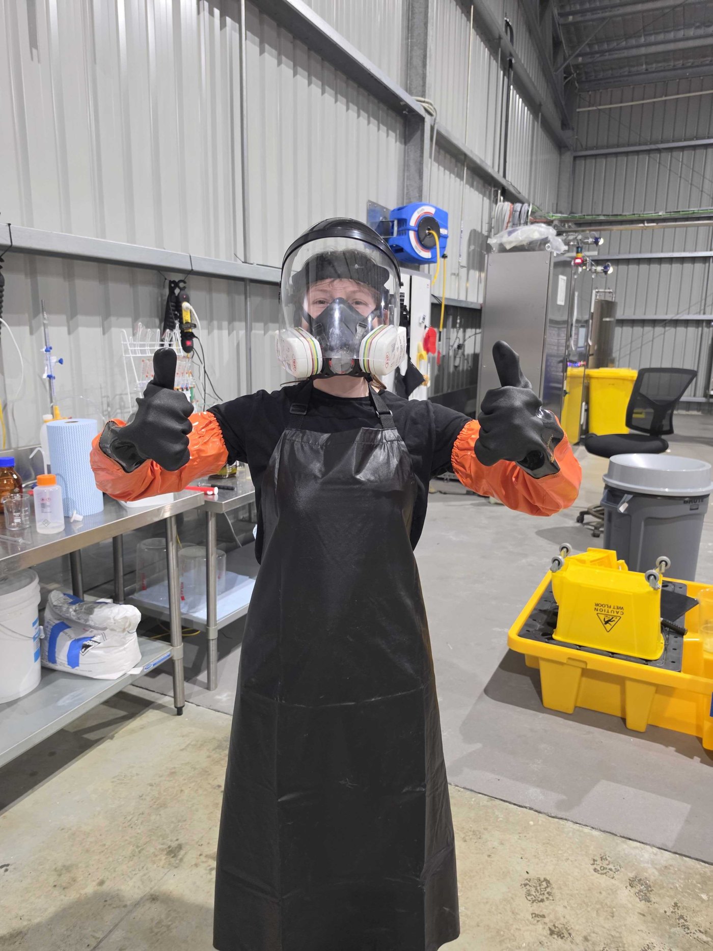 A team member in full safety gear giving two thumbs up in the lab